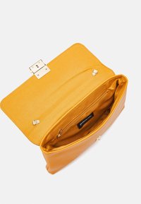 Bolso de cuero amarillo mostaza con forma rectangular, forro de tela, bolsillo interior con cremallera y cierre de hebilla en tono dorado.