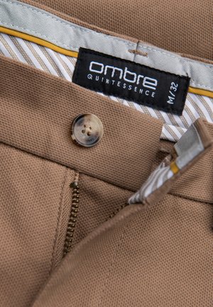 Bruine stoffen broek met een rits en knoopsluiting. Het label geeft "Ombre Quintessence, M/32" aan. De voering heeft een streeppatroon in lichte kleuren.
