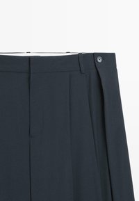 Dunkelgraue Hose mit flacher Vorderseite, einfacher Falte und Knopfverschluss. Verfügt über Seitentaschen und eine glatte Stoffstruktur.