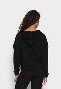 Schwarzer Kapuzenpullover aus weichem, strukturiertem Stoff. Verfügt über lässige Ärmel und eine entspannte Passform, ideal für Freizeitkleidung.