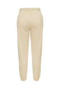 Béžové teplákové nohavice vyrobené z mäkkej látky, s elastickým pásom a manžetami pre pohodlné nosenie, so bočnými vreckami pre praktickosť.