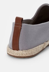 Botte en toile grise avec un accent en cuir marron au niveau du talon et une semelle en jute naturel. Dispose d'un design à l'arrière fermé.