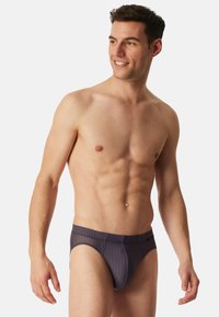 Herren Badebrieftangas in Marineblau mit dünnen orangefarbenen vertikalen Streifen. Hergestellt aus glattem Stoff, mit einem figurbetonten Schnitt und elastischem Bund.
