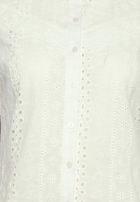 Hvid bluse med broderede detaljer, knappelukning og broderie anglaise-mønstre overalt. Letvægts, struktureret stof.