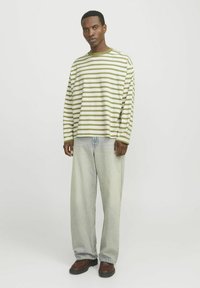 Camisa de manga larga a rayas en verde claro y blanco, combinada con jeans holgados de lavado claro y zapatos marrones; ajuste casual, material de algodón.