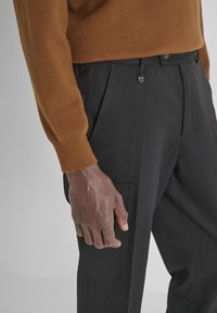 Bruine gebreide trui met ribbels aan de mouwen, gecombineerd met zwarte op maat gemaakte broeken met zijzakken en elastische details in de taille.