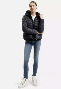 Czarna kurtka puchowa z kapturem, zapinana na zamek błyskawiczny, z pikowanym wzorem. W połączeniu z niebieskimi dżinsami i białymi sneakersami.