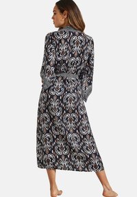 Maxi-rok in marineblauwe stof met een herhalend wit en aardetint patroon, met lange mouwen en een strikdetail in de taille.