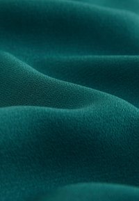 Material de culoare teal cu o suprafață moale și texturată, care prezintă ondulații și pliuri subtile, evidențiind textura sa netedă, dar ușor ridicată.