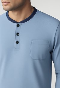 Camicia a maniche lunghe azzurro chiaro con colletto blu scuro, tre bottoni neri e una piccola tasca sul petto con forma rettangolare e bordi cuciti.