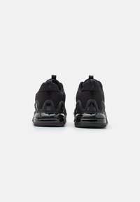 Zapatos deportivos negros con parte superior de malla, suela de goma negra sólida y detalles brillantes en el talón, además de lengüetas para facilitar su puesta.