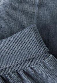 Ribbed knit fabric in muted blue-grey, featuring a prominent elastic waistband and a flared skirt with subtle texture variations.