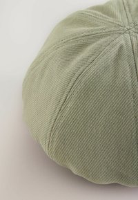 Rund, ribbet pude i en afdæmpet grøn stof, prydet med et syet mønster og blød tekstur, med en fyldig, puffy form.