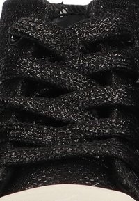 Zapatilla negra texturizada con cordones trenzados y una gruesa suela de goma blanca. Presenta una lengüeta suave y ojales reforzados para mayor durabilidad.