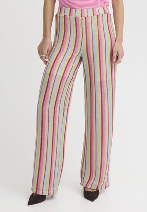 Woman wearing high-waisted, wide-leg pants with vertical stripes in pink, yellow, blue, and cream, paired with pink top and black pointed shoes.