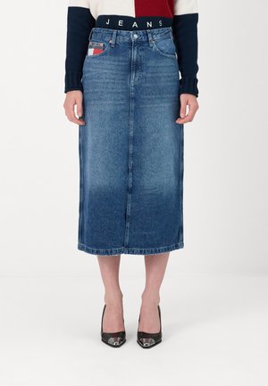 Falda midi de mezclilla en un lavado azul claro a medio, con una abertura frontal, dobladillo cosido y detalles de bolsillo en contraste, combinada con tacones negros.