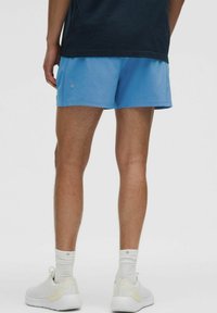 Himmelblaue Sportshorts mit glatter Textur, knielang und mit kleinem Logo-Detail an der Seite, kombiniert mit weißen Sneakers.