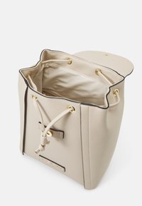 Beige hinkväska i texturerad läder, med guldfärgade detaljer, dragsko-stängning och en mjuk, ljusfodrad insida.