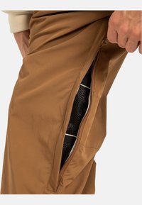 Bruine broek met een zippered zijzak met een mesh voering. De stof heeft een gladde textuur, geschikt voor actieve kleding.