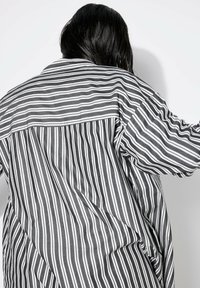 Camicia a maniche lunghe a righe realizzata in tessuto leggero. Presenta righe verticali bianche e nere, vestibilità ampia e colletto classico.