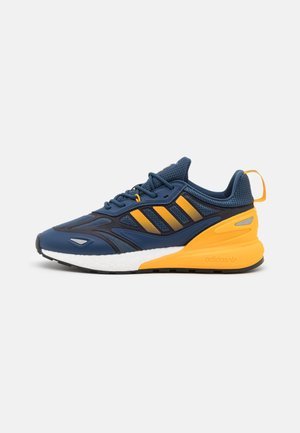 Baskets de sport bleu marine et jaune avec dessus en mesh, fermeture à lacets, semelle blanche et languette à l'arrière.