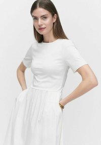 Vit klänning med en figurnära bodice med korta ärmar, en utsvängd kjol och samlad midja. Slät textur med en ren design och inga mönster.