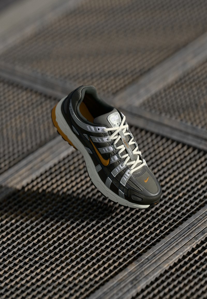 Sapatilha de corrida Nike com parte superior em malha cinza, detalhes brancos e um logotipo laranja brilhante. Apresenta uma sola texturizada e um design acolchoado.