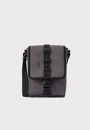 Malá tmavosivá kabelka cez rameno s čiernym remienkom na pracku a nastaviteľným ramenným popruhom s logom značky.