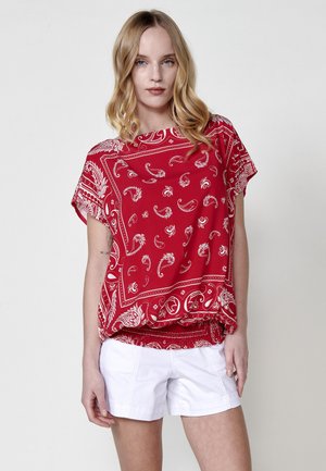 Top rojo de manga corta con patrones de cachemira blancos, de corte holgado y con dobladillo fruncido. Combinado con pantalones cortos blancos. Textura de tela suave.