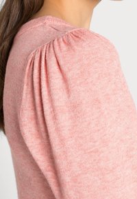 Ljust rosa stickad tröja med rundad halslinning och puffärmar, med en mjuk textur och en figursydd silhuett.