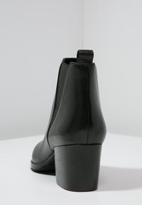 Musta nahkasaapas nilkkapituisella, paksulla korolla, joustavilla sivupaneeleilla ja takana vetoketjulla. Sujuva tekstuuri ja tyylikäs muotoilu.