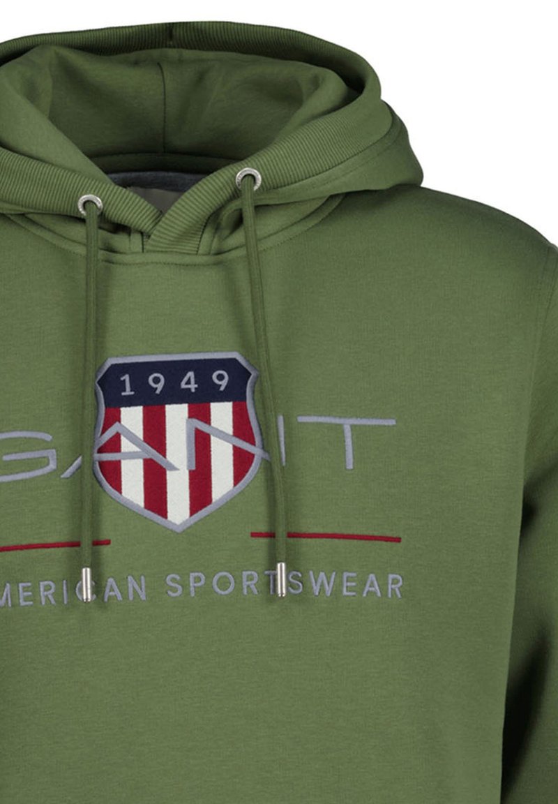 Felpa verde con cappuccio in tessuto morbido, caratterizzata da una toppa con logo frontale a forma di scudo, strisce rosse e bianche e dettagli con coulisse.