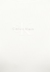 Weißes, geripptes Stoffmaterial mit eingeprägtem Calvin Klein-Logo, das große "CK"-Buchstaben und kleineren Text in der Mitte zeigt.