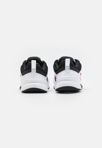 Black and white sneakers with pink accents, featuring a mesh upper, cushioned sole, and a pull tab at the back for easy wearing.