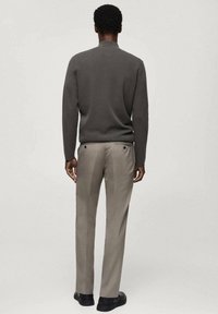 Pull gris foncé à col montant, associé à un pantalon beige clair. Les deux vêtements ont une texture lisse et une coupe ajustée. Chaussures noires visibles.