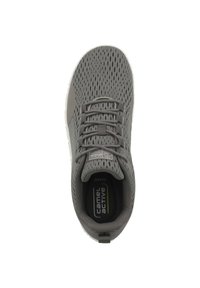 Grauer Sportschuh mit einem Mesh-Obermaterial, das Perforationen aufweist, flachen Schnürsenkeln und einer gepolsterten weißen Außensohle. Das Innere enthält ein Logodesign.