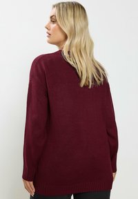 Suéter de punto burdeos con mangas largas, puños y dobladillo acanalados. Textura suave, corte holgado y escote redondo.