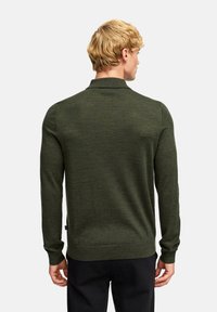 Dunkelgrüner Pullover mit langen Ärmeln, geripptem Kragen und Bündchen, der eine glatte Stricktextur und einen subtilen Glanz aufweist.