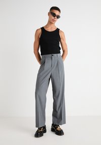 Débardeur noir, pantalon large gris avec plis devant, et bottes noires épaisses avec un motif à pois. Modèle portant des lunettes de soleil.
