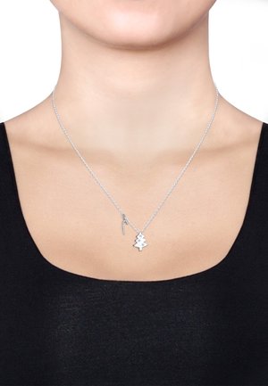 Zilveren ketting met een boomhanger die twee sterren bevat, een getextureerde ketting en een kleine accenthanger. G gedragen over een zwarte top.