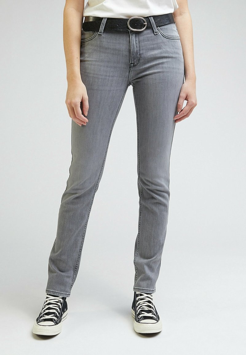 Jean en denim gris à coupe slim, doté d'une taille haute, de coutures discrètes et d'une ceinture noire. Associé à des baskets noires et blanches.
