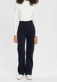 Granatowe spodnie kordowe z wysokim stanem, szerokimi nogawkami i przednimi kieszeniami, zestawione z białym golfem z długim rękawem i białymi trampkami.