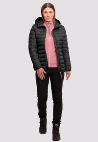 Chaqueta de plumas negra con capucha, textura acolchada, detalle de cremallera plateada, sobre una camiseta rosa con cremallera. Combinada con pantalones negros y botas marrones.