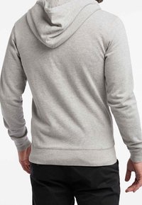 Felpa grigia realizzata in un materiale morbido, con cappuccio regolabile tramite cordino, polsini e orlo a coste. Texture liscia con dettagli di cucitura minimi.