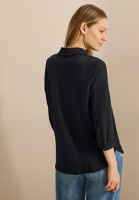 Schwarzes strukturiertes Langarmhemd mit Kragen und umgeschlagenen Bündchen, kombiniert mit hellblauen Jeans. Erhältlich in einer lockeren Passform.