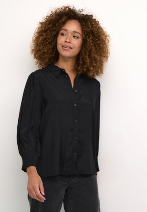 Chemise noire boutonnée avec un col, des manches bouffantes longues et des poignets smockés. Fabriquée dans un tissu lisse avec une finition brillante.