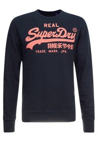Sudadera azul marino de algodón, con un gran texto gráfico rosa "REAL SuperDry" en el frente y puños y dobladillo acanalados.