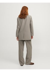 Costume gris clair comprenant un long blazer avec un dos fendu et un pantalon à jambes larges assorti. Tissu lisse avec des lignes épurées et un minimum de détails.