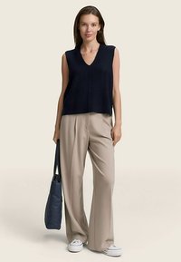 Top senza maniche blu navy a coste con scollo a V, abbinato a pantaloni beige chiaro a gamba larga e scarpe slip-on bianche, completato da una borsa blu.