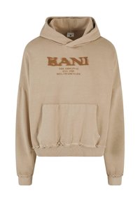 Sweatshirt à capuche beige avec une poche frontale, présentant des ourlets effilochés et du texte de marque imprimé en marron. Matériau en coton doux.